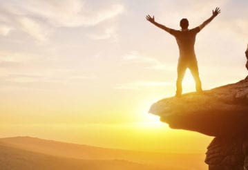 Man with his arms up, stand on a cliff